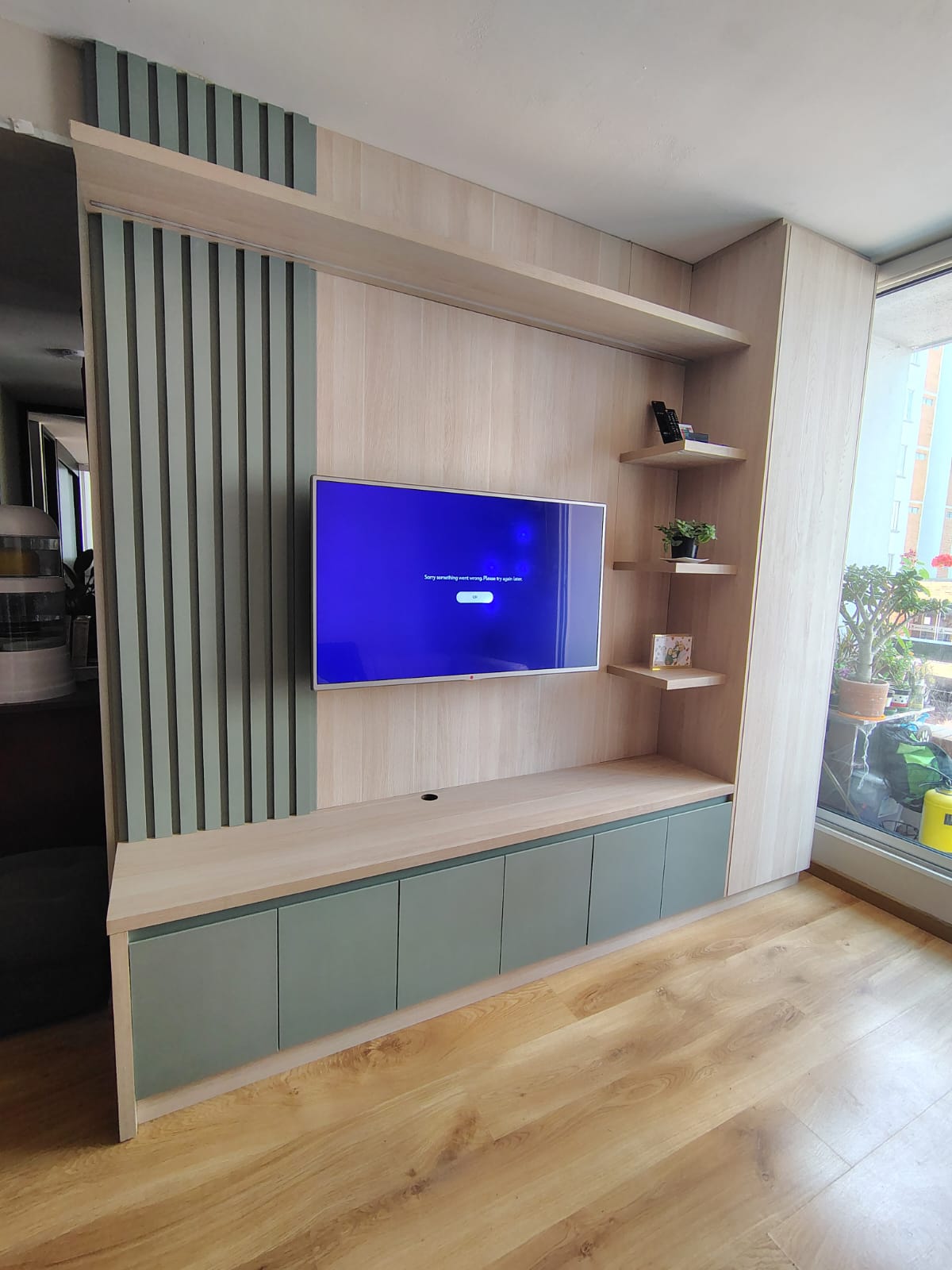Mueble de TV en madera con panel decorativo y gabinetes en verde salvia, instalado en Bogotá
